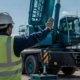 Qualified crane signal person in high-visibility vest giving standard hand signals to a crane operator on a construction site