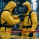 Two HAZWOPER workers in Level B chemical protective suits conducting pre-entry buddy inspection before hot zone entry