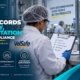 Batch records accuracy documentation and safety compliance guide showing a pharmaceutical manufacturing worker in a white lab coat, hair net, and blue gloves completing a batch record checklist covering materials, process steps, in-process checks, test results, and approvals on a clipboard, with master batch records, batch production records, quality control records, deviation records, change control, and training records binders stacked beside the workstation in a GMP facility
